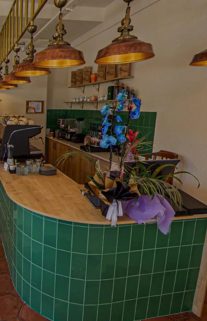 Adagan Kafe’nin iç kısmında yer alan yeşil seramik kaplı bar alanı, dekoratif aydınlatmalar ve canlı çiçeklerle öne çıkıyor.